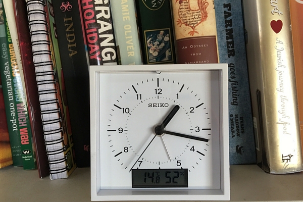 Clock sitting on shelf next to recipe books