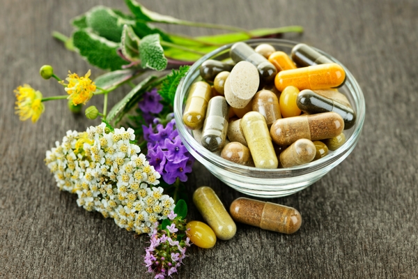 Bowl of supplements alongside fresh herbs