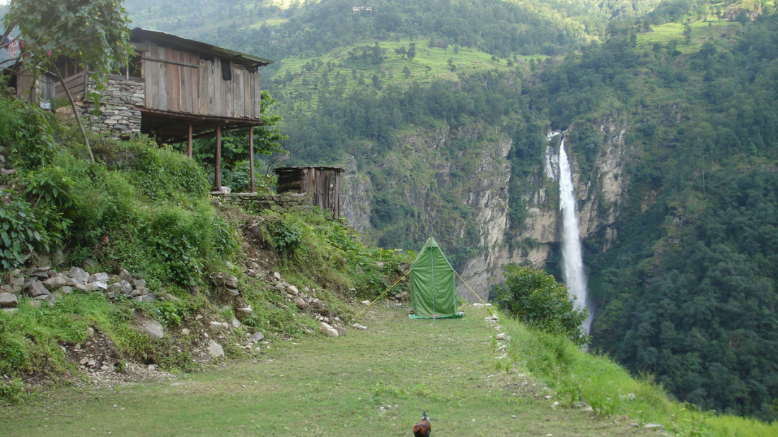 Camp ground at Soti Khola with waterfall and wooden houses