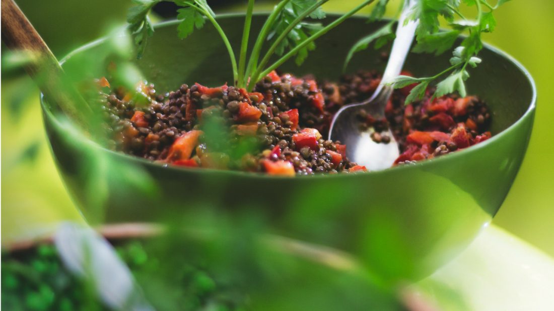 Bright green bowl of brown lentil and quinoa salad with tomato and herbs