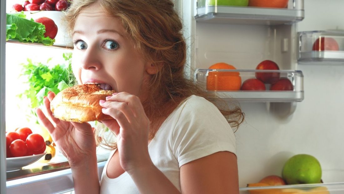 Woman eating pastry in front of open refridgerator